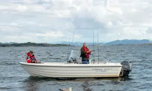 Zwei Männer genießen das Angeln in Norwegen auf einem Boot. Eine Möwe schwimmt im Wasser.