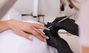 Manicurezystka w czarnych rękawiczkach przygotowuje paznokcie do stylizacji. Zastanawiasz się, czy można mieszać lakiery hybrydowe?