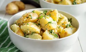 Una ciotola bianca piena di saporita insalata di patate napoletana, condita con prezzemolo fresco e aglio.