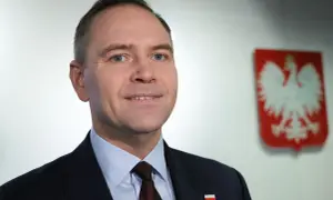 Polityk w garniturze z polskim godłem w tle.