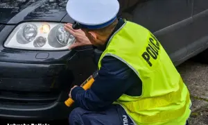 Policjant sprawdza światła samochodu, w tym światła przeciwmgielne. W ręku trzyma miernik.