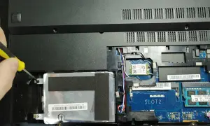 Ręka przykręca śrubkę mocującą dysk SSD w laptopie. Poradnik: jak zamontować dysk SSD.