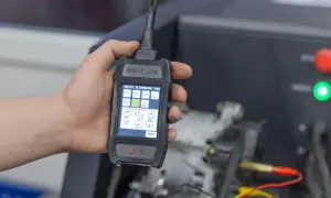 Dłoń trzyma tester diagnostyczny do alternator w samochodzie. Ekran pokazuje wybór typu alternatora i połączeń LIN/BSS.