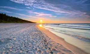 Zachód słońca nad morzem, piaszczysta plaża z odciskami stóp, las w tle. Idealne, fajne miejsce nad morzem dla dwojga na romantyczny spacer.