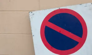 Znak b35 zakazu zatrzymywania się, czerwone koło z niebieskim polem i czerwoną przekątną, przykręcony do jasnej ściany.