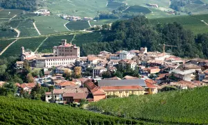 Colline verdi delle Langhe, con vigneti rigogliosi che circondano un borgo dominato da un castello. L'atmosfera evoca la produzione del pregiato Barolo.