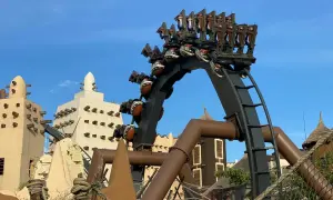 A roller coaster with brown seats and patterned spheres against a blue sky and themed buildings.