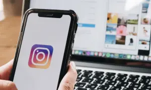 Telefon z logo Instagrama w dłoni, obok laptop z otwartą aplikacją. Dowiedz się, jak zmienić dźwięk powiadomień na Instagramie.