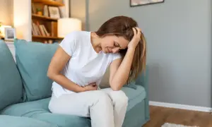 Femme assise sur un canapé bleu, se tenant le ventre et la tête, visiblement souffrante. Elle pourrait exprimer la douleur liée à l'endométriose profonde.