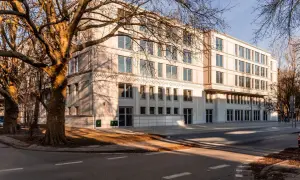 Nowoczesny budynek mieszkalny z dużymi oknami i drzewami w pobliżu, w słoneczny dzień.