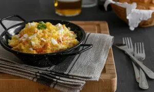 Una deliciosa ensalada rusa, cremosa y con trozos de huevo duro y zanahoria, servida en un cuenco negro.