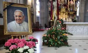 Obraz ojca świętego Franciszka w kościele, otoczony kwiatami i krzyżem.