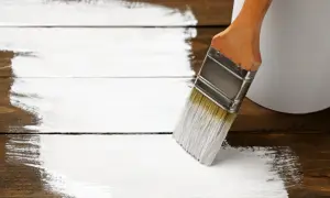 Pędzel maluje drewniany stół na biało. Zastanawiasz się, czym pomalować stół drewniany? Biała farba nada mu nowy wygląd.
