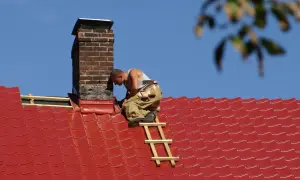 Handwerker dichtet den Schornstein am roten Ziegeldach ab.