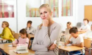 Nauczycielka zamyślona w klasie, gdzie uczniowie piszą. Czy to kolejna lekcja, czy może czas na nadgodziny nauczycieli?