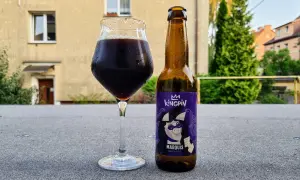 Kieliszek ciemnego piwa miodowego obok butelki Kingpin Marquis.