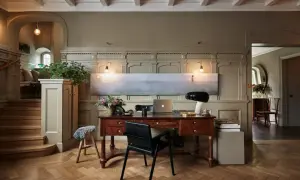 Ett elegant skrivbord med laptop och lampa, i en hall med trappa och konst. Martin Brudnizki-inspirerad design.