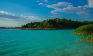 Turkusowe jezioro i las tworzą krajobraz jak z Malediwów w Polsce. W oddali widać komin fabryki.