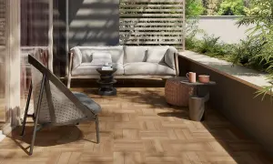 Terrazzo con pavimenti in gres porcellanato effetto legno, arredato con divano, poltrona e tavolini, immerso nel verde.