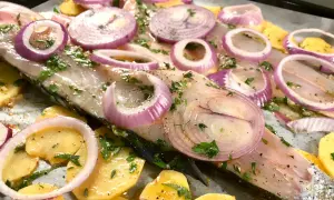 Lavarello in padella pronto per la cottura, con patate affettate, cipolla rossa a rondelle e prezzemolo fresco.