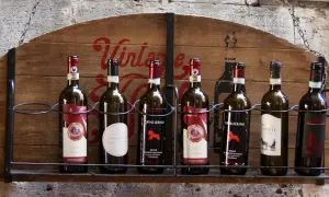 Rząd butelek wina z Toskanii, w tym Chianti Classico i Rosso Montepulciano, na drewnianej półce.