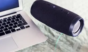 Un ordinateur portable et une enceinte Bluetooth noire sur une table en verre. Apprenez comment connecter une enceinte Bluetooth pour une expérience audio sans fil.