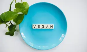 Niebieski talerz z literami "VEGAN" i zielonymi liśćmi. To symbol tego, co to jest weganizm – dieta bez produktów odzwierzęcych.