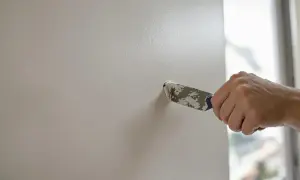 Main tenant utilise un couteau à mastic pour reboucher un trou dans un mur blanc.
