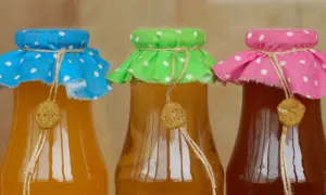 Trzy butelki z domową miodosytnią, każda ozdobiona kolorową tkaniną w kropki i sznurkiem.