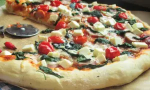 Pyszna pizza ze szpinakiem, pomidorkami koktajlowymi i kostkami sera feta. Idealna na szybki obiad.