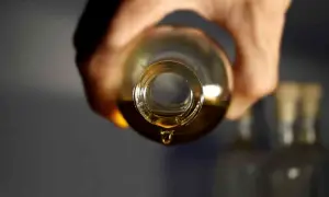 Une goutte d'huile dorée tombe d'une bouteille, parfait pour votre huile cheveux maison.