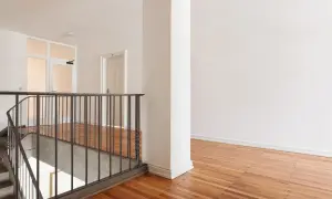 Jak pomalować wysoką klatkę schodową? Jasne wnętrze z drewnianą podłogą i metalową balustradą.