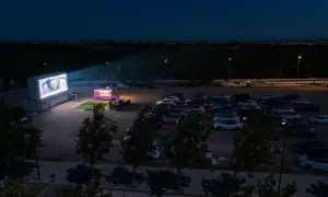Noche de cine de verano Zaragoza. Coches aparcados frente a una gran pantalla donde proyectan una película, con un camión de comida rosa al lado.