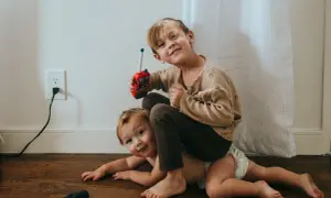 Twee broertjes spelen op de grond. De oudste zit op de rug van de jongste en houdt een speelgoedwalkietalkie vast. Dit is waarom maken broers en zussen ruzie.