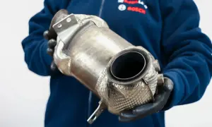 Mechanik w rękawiczkach trzyma katalizator samochodowy, element układu wydechowego, który pomaga ograniczyć emisję szkodliwych substancji.