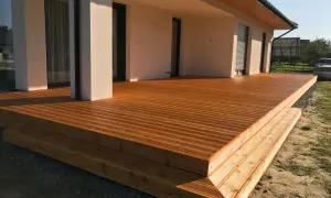 Nowa, drewniana terasa z widocznymi stopniami, zabezpieczona impregnatem do legarów tarasowych, lśni w słońcu.