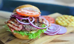 Burger z bekonem, sałatą, pomidorem i czerwoną cebulą na desce.