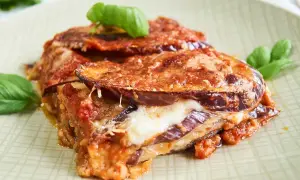 Parmigiana di Melanzane auf einem Teller mit Basilikum garniert.