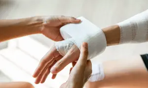 Opatrywanie dłoni po urazie, aby zapobiec martwicy skóry. Białe bandaże owijają nadgarstek i kciuk.