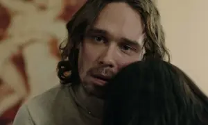 En man med långt hår och blå ögon kramar någon i tv-serien "Rollistan i Knutby".
