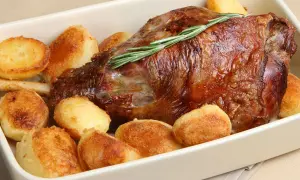 Succulento agnello al forno con patate arrosto dorate, guarnito con rosmarino fresco.