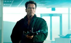 Arnold Schwarzenegger w zielonej kurtce z karabinem, gotowy do akcji w jednym ze swoich kultowych filmów.