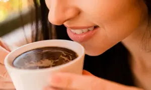 Uśmiechnięta kobieta delektuje się aromatyczną kawą po wszczepieniu implantu.