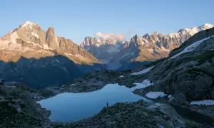 Un randonneur solitaire admire le reflet des Aiguilles Rouges dans un lac d'altitude. Le soleil couchant éclaire les sommets enneigés.