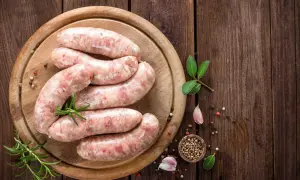 Surowa biała kiełbasa na desce, z ziołami i przyprawami. Zastanawiasz się, jak długo parzyć kiełbasę białą?