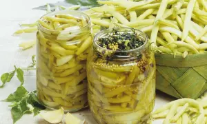 Zwei Gläser mit eingelegten Buschbohnen, daneben frische Bohnen und Knoblauch.