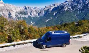 Blauer Campervan auf Bergstraße in Albanien. Perfektes Wetter im August für eine Reise durch die beeindruckende Berglandschaft.