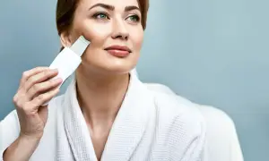 Kobieta w szlafroku wykonuje peeling kawitacyjny w domu, odświeżając cerę.