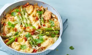 Herzhafter Spargel Auflauf mit Kartoffeln, Speck und geschmolzenem Käse, garniert mit Petersilie und Zitronenschale.