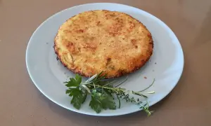 Frittata di cous cous dorata e croccante, guarnita con erbe aromatiche fresche su un piatto azzurro.